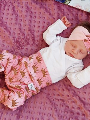 Heleroosa kroonikestega puuvillane keeruga peapael ja beebipüksid vastsündinul, pehme käsitöö beebiteki peal.